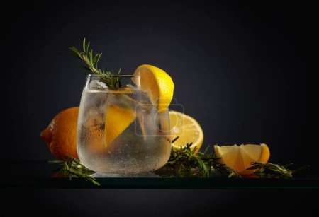 Cocktail gin tonic avec glace, citron et romarin dans un verre congelé. Une boisson rafraîchissante glacée en verre brumeux sur fond noir.