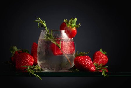 Foto de Cóctel gin tonic con hielo, fresas y romero en un vaso congelado. Una bebida refrescante helada en vidrio nebulizado sobre un fondo negro. - Imagen libre de derechos
