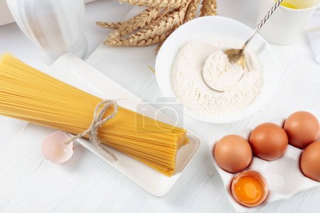 Téléchargez les photos : Spaghetti avec des ingrédients sur une table en bois blanc. - en image libre de droit