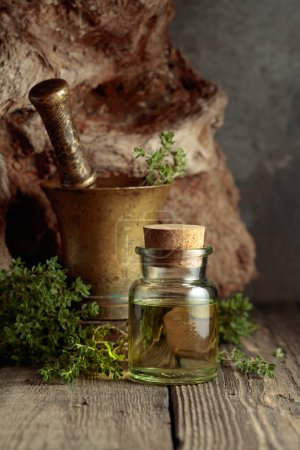 Téléchargez les photos : Bottle of thyme essential oil with fresh thyme twigs on an old wooden table. - en image libre de droit