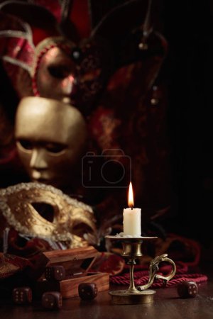 Foto de Vela ardiente, dados y máscaras de carnaval en una vieja mesa de madera. - Imagen libre de derechos