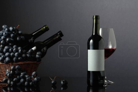 Foto de Red wine and blue grapes on a black reflective background. Focus on an empty label. Copy space. - Imagen libre de derechos
