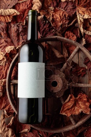 Téléchargez les photos : Bottle of red wine on the rusty wheel and dried-up vine leaves. Old expensive wine concept. Top view. - en image libre de droit