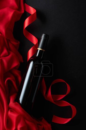 Foto de Bottle of red wine with red satin on a black background. Top view. - Imagen libre de derechos