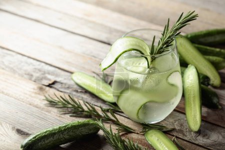 Photo for Gin tonic with ice, rosemary, and cucumber slices in frosted glass. Cocktail with ingredients on an old wooden table. Copy space. - Royalty Free Image