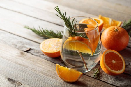 Photo for Gin tonic with ice, rosemary,  and orange slices in frosted glass. Cocktail with ingredients on an old wooden table. Copy space. - Royalty Free Image