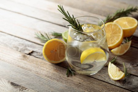 Téléchargez les photos : Gin tonic avec glace, romarin et tranches de citron en verre dépoli. Cocktail avec des ingrédients sur une vieille table en bois. Espace de copie. - en image libre de droit