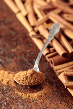 Cinnamon powder in a spoon and cinnamon sticks on a brown background. 
