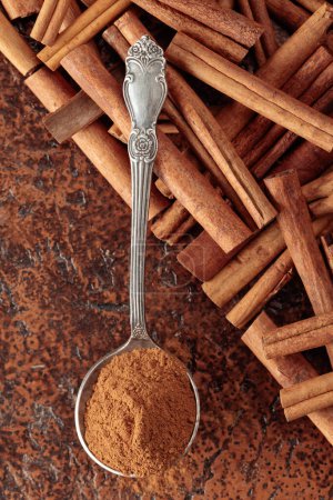 Téléchargez les photos : Poudre de cannelle dans une cuillère et bâtonnets de cannelle sur un fond brun. Vue du dessus. - en image libre de droit