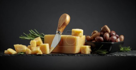 Foto de Parmesan cheese with knife, olives and rosemary on a black background. - Imagen libre de derechos