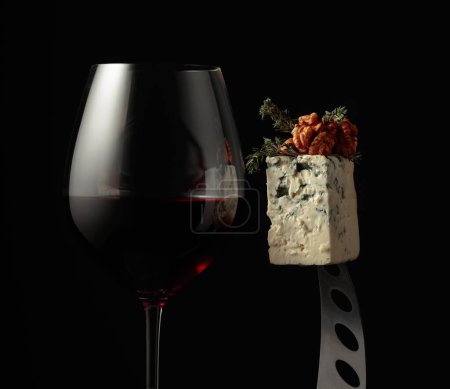 Foto de Un vaso de vino tinto y queso azul. Queso con nueces y tomillo en un cuchillo. - Imagen libre de derechos