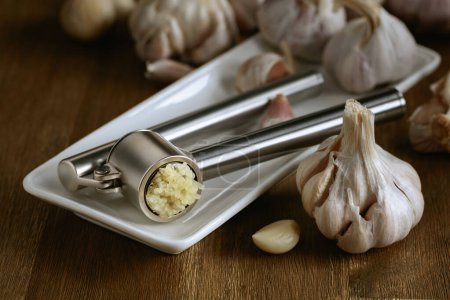 Foto de Garlic bulbs and garlic press on an old wooden table. - Imagen libre de derechos