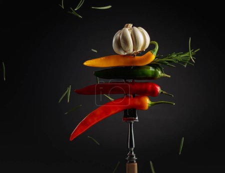 Foto de Red hot chili peppers with garlic and rosemary on a fork. Concept of spicy food. - Imagen libre de derechos