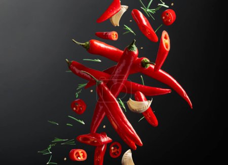 Foto de Especias en movimiento. Cayendo pimientos rojos, ajo y romero sobre un fondo negro. Concepto de comida picante. - Imagen libre de derechos