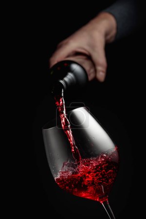 Téléchargez les photos : Verser du vin rouge dans un gobelet de verre. Fond noir avec espace de copie. - en image libre de droit