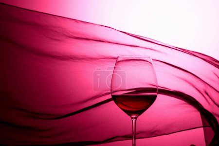 Téléchargez les photos : Verre de vin rouge sur fond de rideau de satin ondulé. Rétro-éclairage rouge. - en image libre de droit