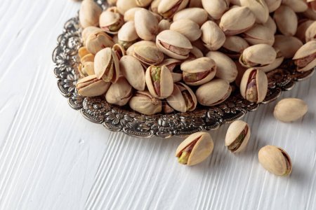 Téléchargez les photos : Salted pistachios in a dish on a white wooden table. - en image libre de droit