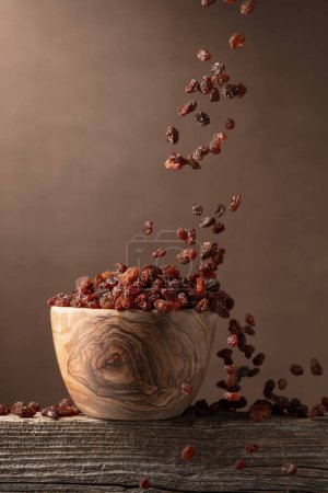 Téléchargez les photos : Voler raisins secs sur un fond brun. Raisins dans un bol en bois. Espace de copie. - en image libre de droit