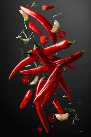 Photo for Falling red chili peppers, garlic, and rosemary on a black background. Spices in motion. Concept of spicy food. - Royalty Free Image