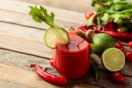 Photo for Bloody Mary cocktail garnished with gherkin, olive, lime, and celery. Tomato drink with ingredients on an old wooden table. - Royalty Free Image