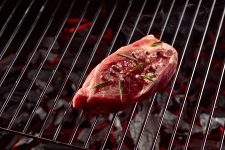 Photo for Raw steak on a grill with rosemary, pepper, and salt. - Royalty Free Image