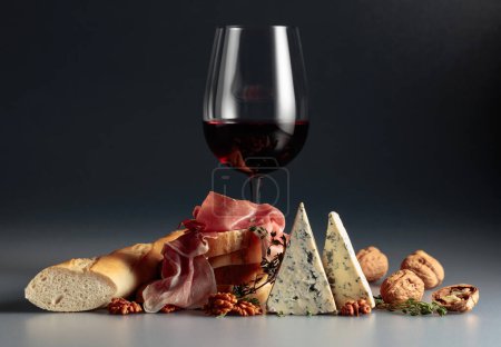 Foto de Prosciutto con queso azul, vino tinto, baguette, nueces y tomillo. Vino tinto con aperitivos tradicionales mediterráneos. - Imagen libre de derechos