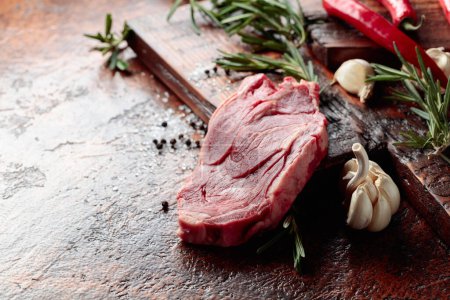 Téléchargez les photos : Steak de viande de bœuf cru avec romarin, ail, sel et poivre sur une vieille table brune. - en image libre de droit