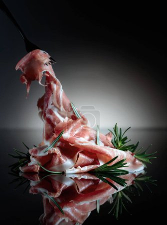 Photo for Italian prosciutto or Spanish jamon with rosemary on a black background. Copy space. - Royalty Free Image