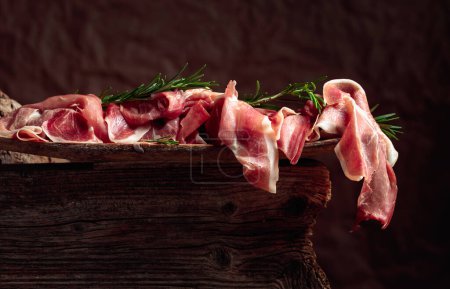 Photo for Italian prosciutto crudo or Spanish jamon with rosemary on an old wooden background. - Royalty Free Image