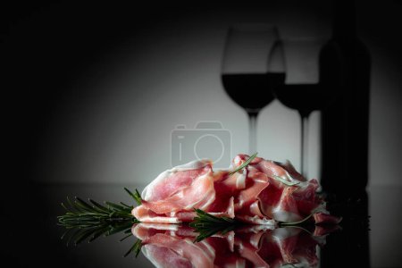 Téléchargez les photos : Italian prosciutto or Spanish jamon with rosemary and red wine on a black background. - en image libre de droit