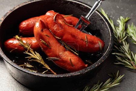 Photo for Roasted Bavarian sausages with rosemary in an old black pan. - Royalty Free Image