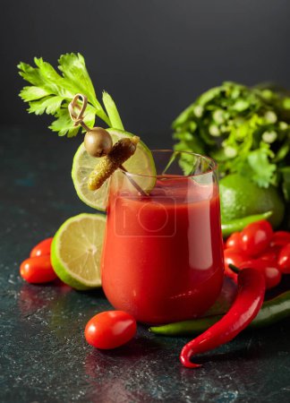 Photo for Bloody Mary cocktail garnished with gherkin, olive, lime, and celery. Tomato drink with ingredients on a black background. - Royalty Free Image