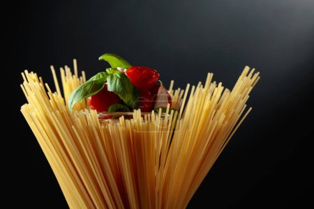 Photo for Raw spaghetti with tomato, garlic, and basil on a black background. - Royalty Free Image