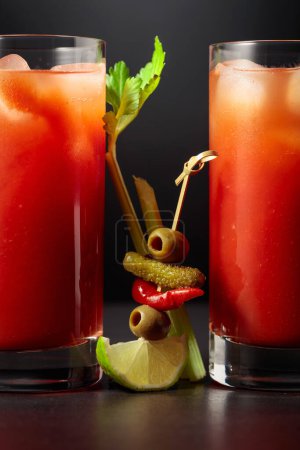 Foto de Cóctel Bloody Mary con apio, pepinillo, aceituna, lima y pimiento rojo. Bebida de tomate sobre fondo negro. - Imagen libre de derechos