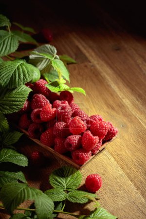 Foto de Ripe juicy raspberries with leaves. Berries in a wooden dish on an old wooden table. - Imagen libre de derechos