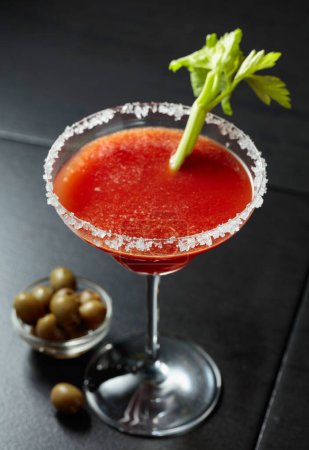 Foto de Bloody Mary cóctel con apio y aceitunas verdes. El vidrio está decorado con sal marina. - Imagen libre de derechos