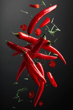 Photo for Falling red chili peppers and rosemary on a black background. Spices in motion. - Royalty Free Image