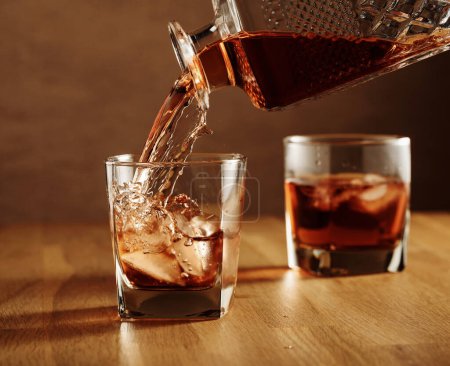 Foto de El whisky se vierte en un vaso embalsado con hielo natural. Un vaso de whisky en una mesa de roble. - Imagen libre de derechos