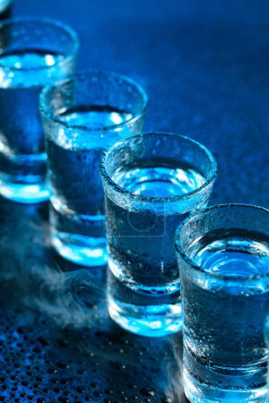 Foto de Los vasos mojados del vodka en el humo sobre el fondo azul oscuro. Enfoque selectivo. - Imagen libre de derechos