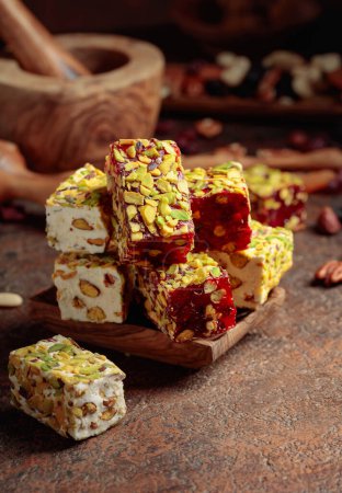 Photo for Turkish delight with nuts and dried fruits. Traditional east sweets on an old brown table with wooden kitchen utensils. - Royalty Free Image