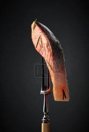 Téléchargez les photos : Smocked salmon on a fork. Fish piece on a black background. - en image libre de droit