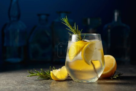 Foto de Cóctel gin tonic con hielo, romero y limón sobre una mesa de piedra en un bar. - Imagen libre de derechos