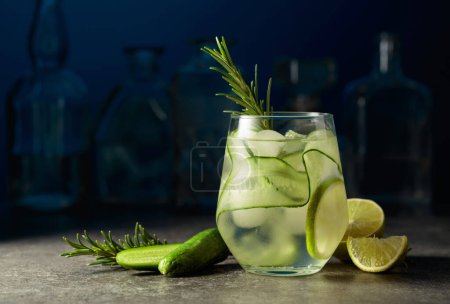 Téléchargez les photos : Cocktail gin tonic avec glace, romarin, lime et concombre sur une table en pierre dans un bar. - en image libre de droit