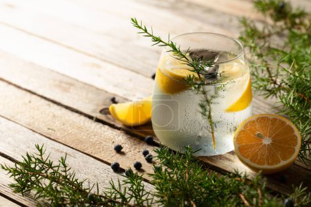 Foto de Cóctel de Gin tonic con limón, ramas de enebro y bayas. Cóctel en un vaso con hielo sobre una mesa de madera rústica, espacio para copiar. - Imagen libre de derechos