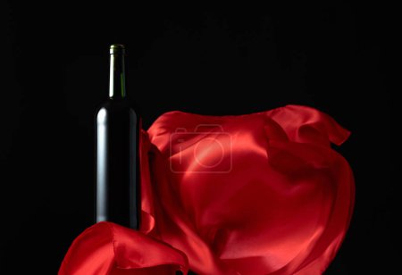 Téléchargez les photos : Bouteille de vin rouge et volutes de tissu rouge sur fond noir. - en image libre de droit