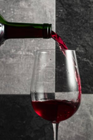 Foto de El vino tinto se vierte de la botella en una copa. Fondo de piedra gris y negro. - Imagen libre de derechos