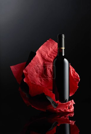 Photo for Bottle of red wine on a crumpled paper. Black reflective background. - Royalty Free Image