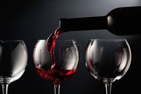 Téléchargez les photos : Verser du vin rouge dans un verre à vin sur fond noir. - en image libre de droit