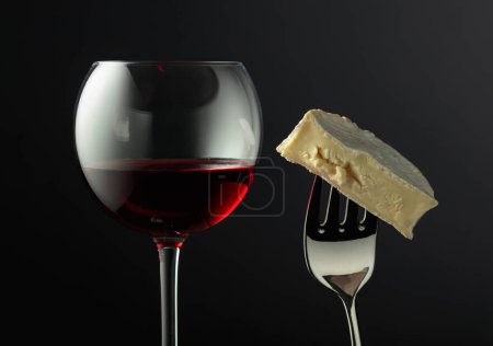 Photo for Glass of red wine and Camembert cheese on a fork. - Royalty Free Image