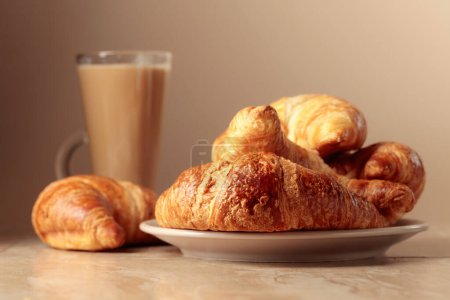 Photo for Freshly baked croissants and coffee with cream on a beige ceramic table. - Royalty Free Image